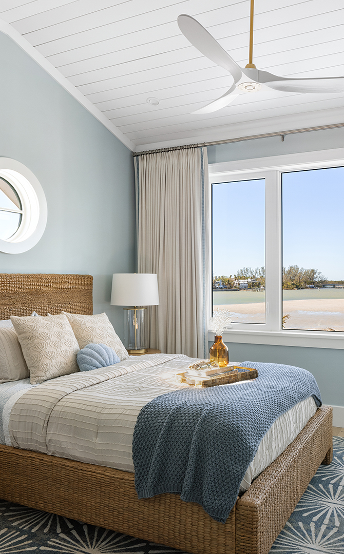 Coastal-themed bedroom with a wicker bed, large window, and beach view featuring walls painted Niebla Azul and Pure White trim.