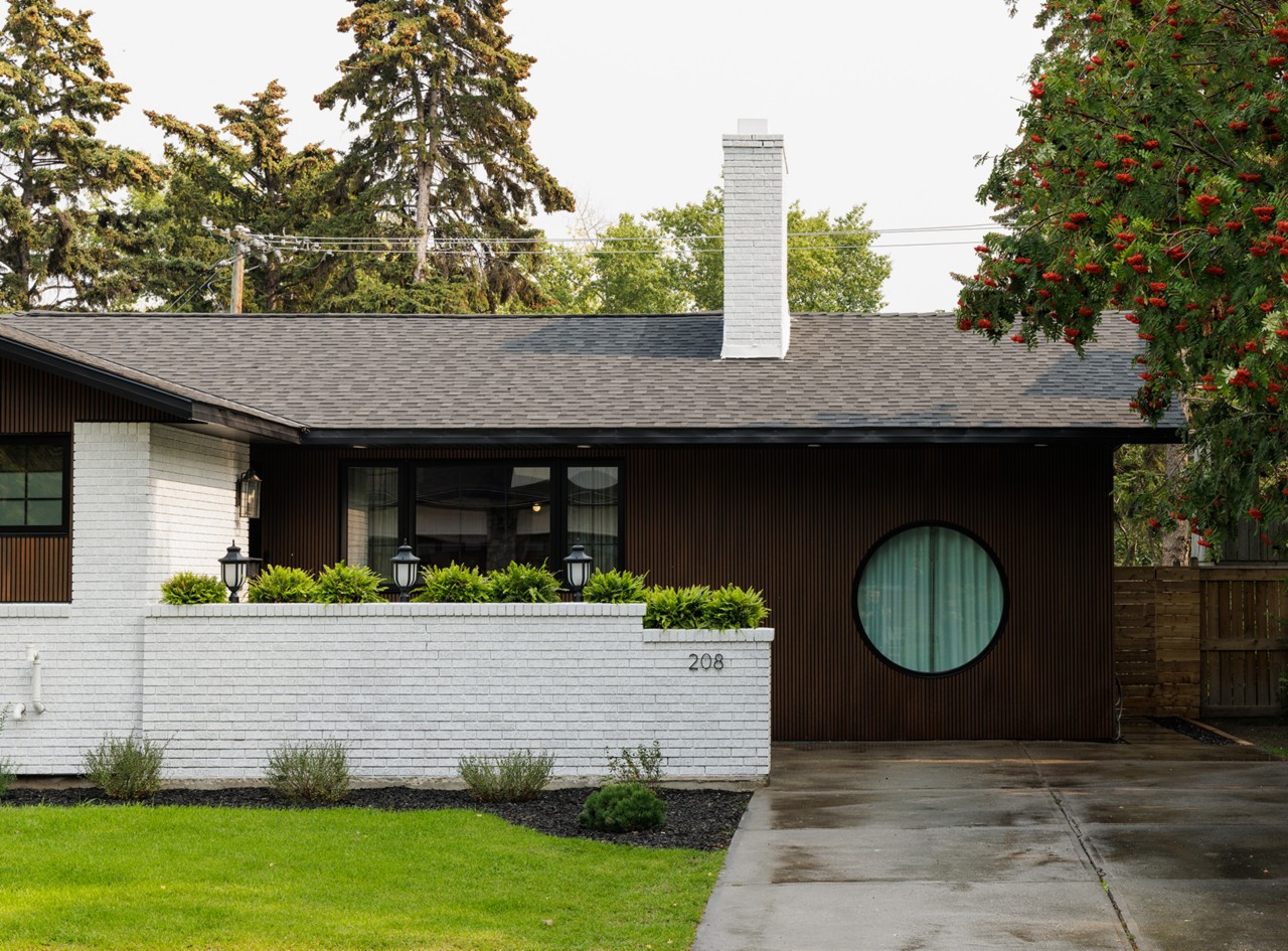 Exterior of Aly and Jason’s house with white brick and dark wood facade, circular window, and white chimney.
