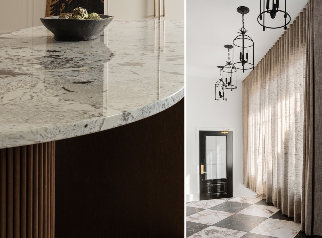 Close-up of the curved kitchen island countertop with a bowl and a room with lantern-style pendant lights, floor-to-ceiling curtains, and marble tile flooring bathed in natural light.
