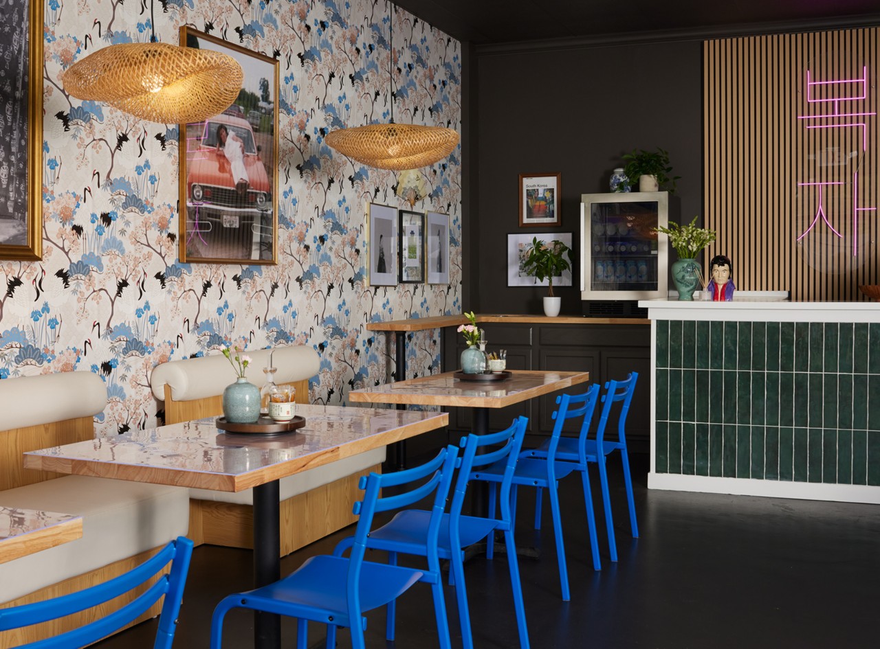 A café interior with blue chairs, wooden tables, floral wallpaper, and a green tiled bar.