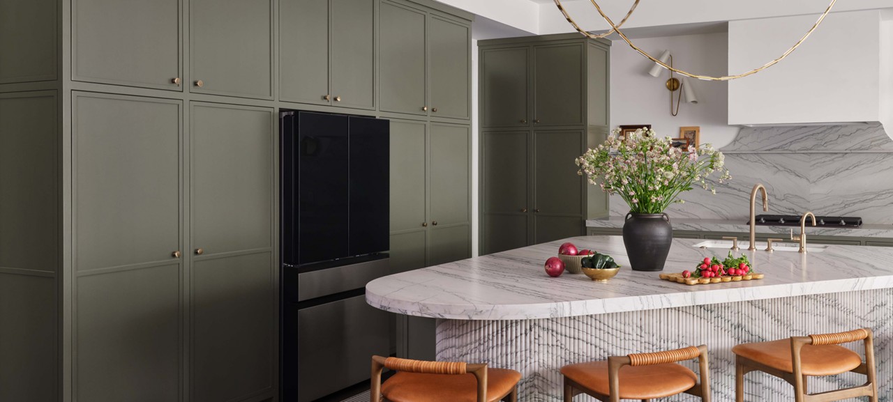 Modern kitchen with a marble island, dark green cabinets, and warm accents. 