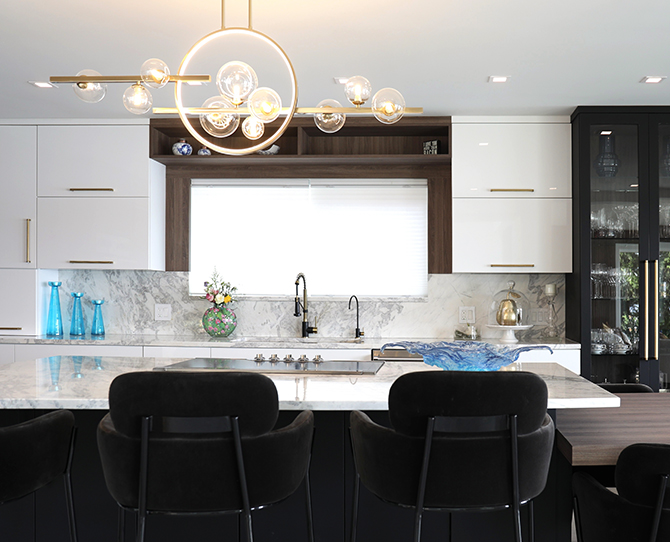 Modern kitchen with white cabinets, marble island, and chandelier.