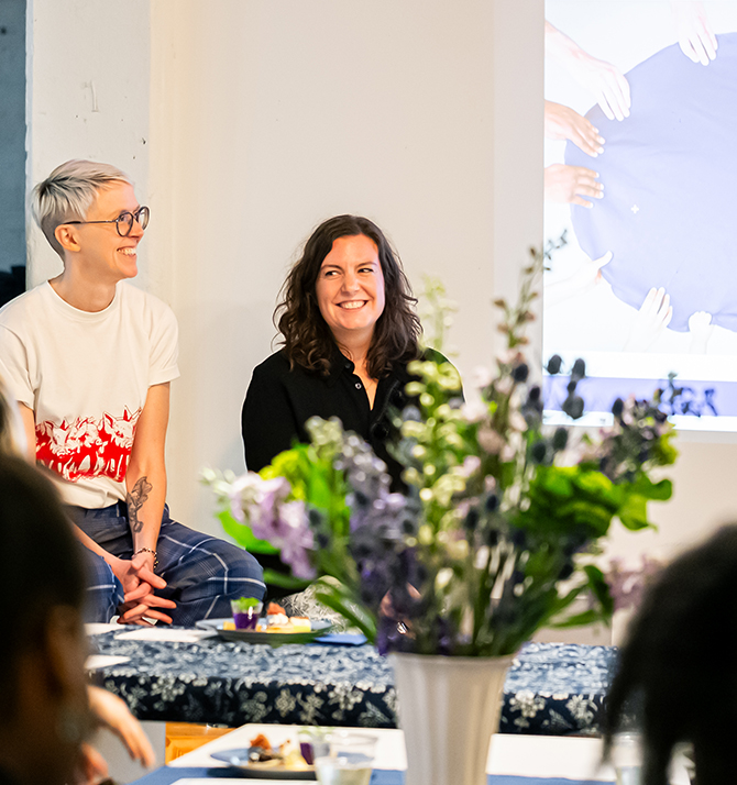 The Taste Curators smiling in front of a projected image, with flowers in the foreground.