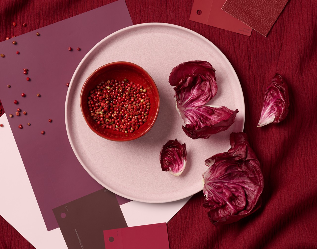 Flatlay image of a bowl of pink peppercorns and radicchio leaves on a plate surrounded by Sherwin-Williams paint samples in similar colors.