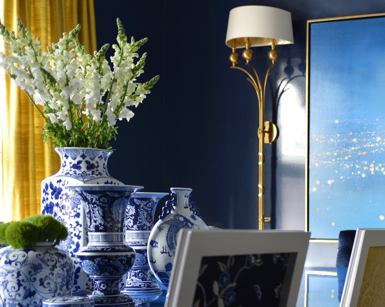Blue and white porcelain vases with flowers, next to a gold lamp and a blue gradient painting with walls painted Gale Force by Sherwin-Williams.