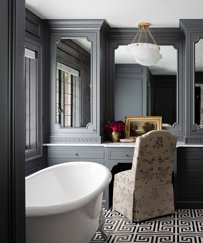 A luxurious gray bathroom with a white bathtub, marble double vanity, ornate mirrors, and a geometric floor pattern with walls painted Roycroft Pewter.