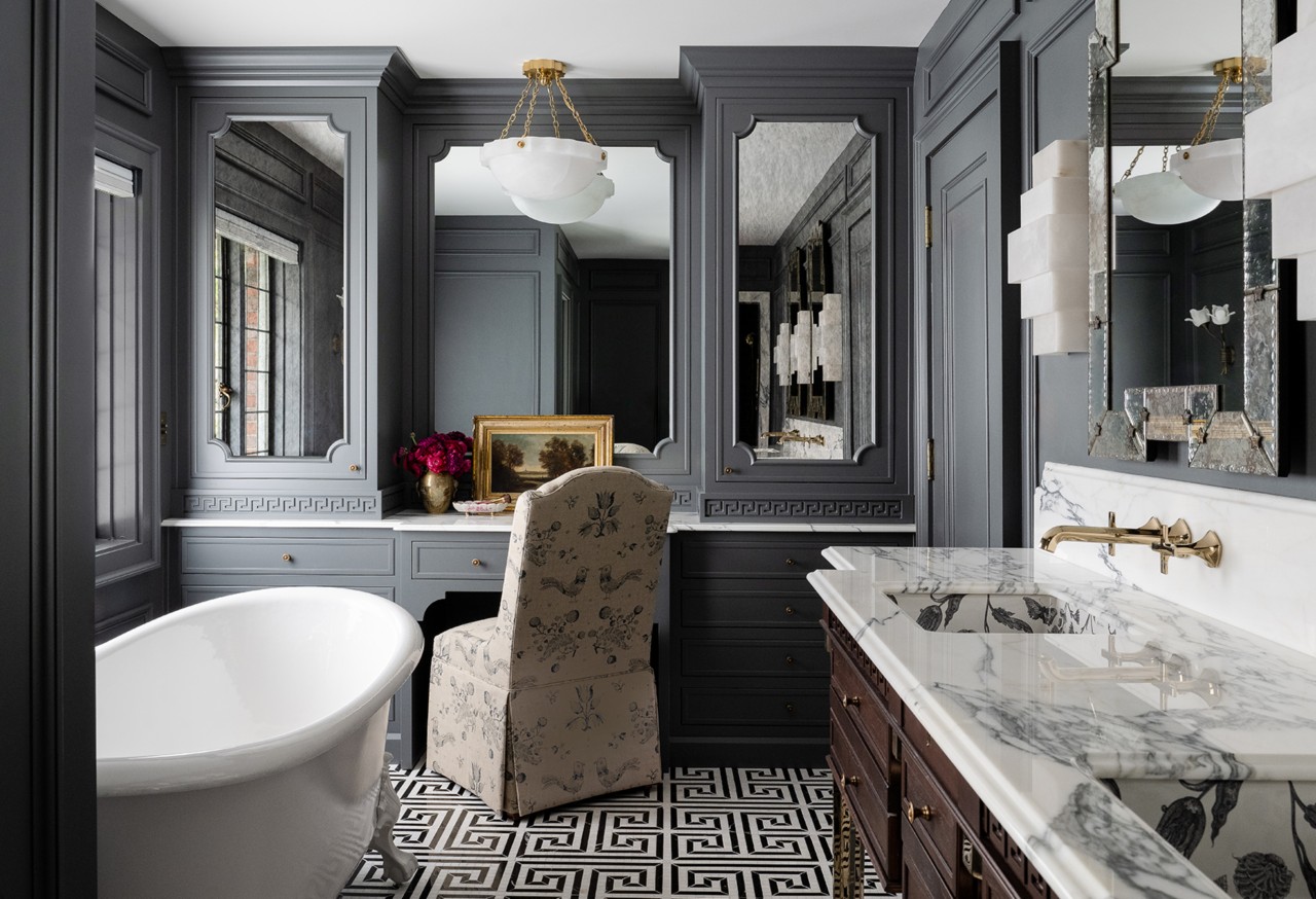 A luxurious gray bathroom with a white bathtub, marble double vanity, ornate mirrors, and a geometric floor pattern with walls painted Roycroft Pewter.