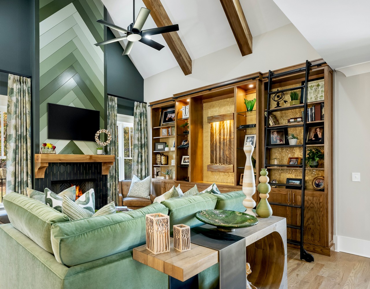 A modern living room with a green-accented fireplace, green sectional sofa, wooden shelves, and vaulted ceiling with wooden beams.