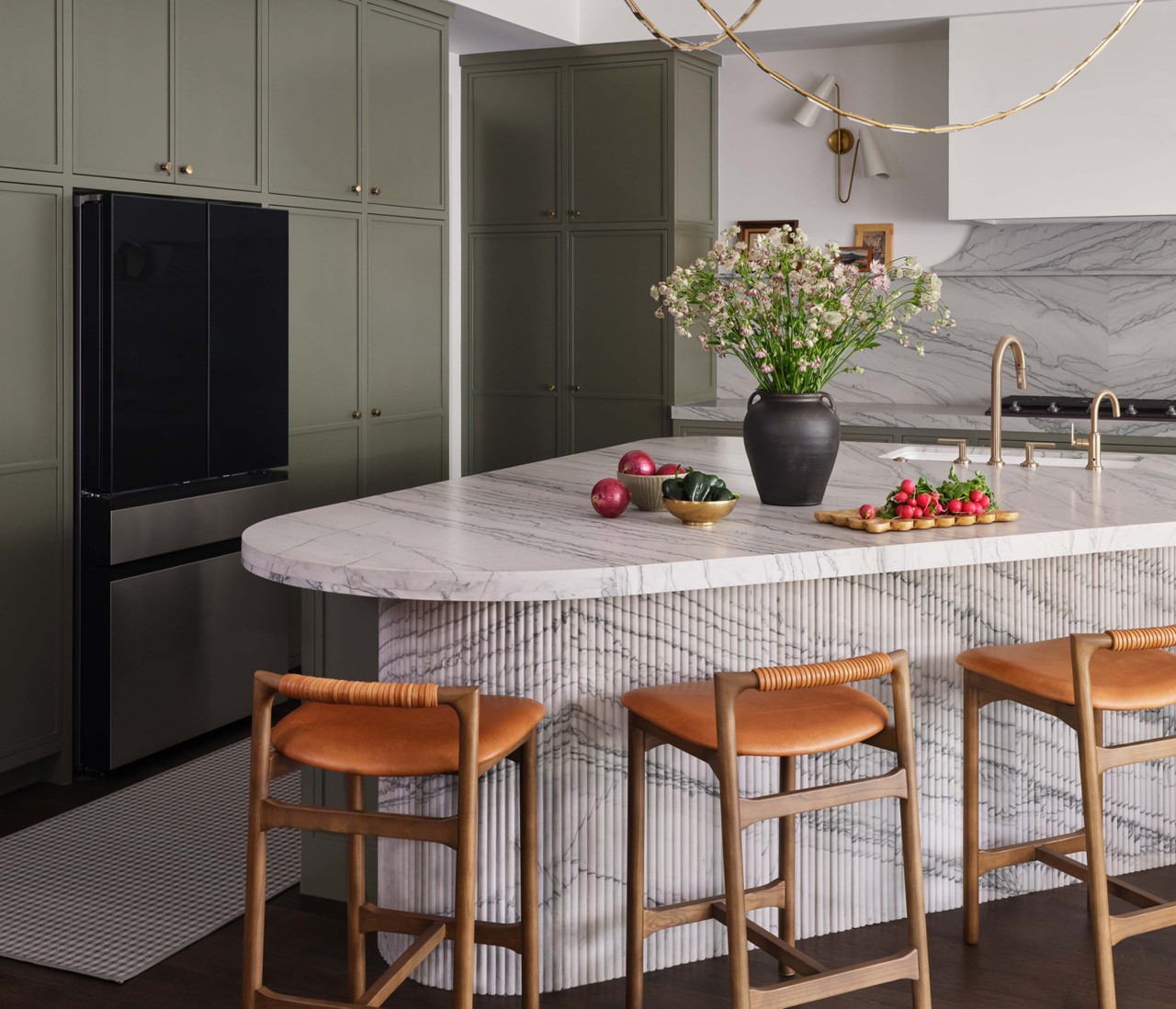 Modern kitchen with marble backsplash and island topped with vase of flowers and fresh vegetables, and Roycroft Bronze Green perimeter cabinets.