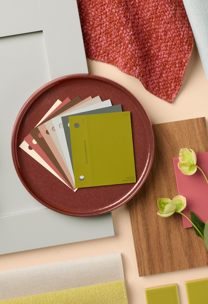 A round dish with paint color samples for The Loneliest Color 2026 coordinating palette surrounded by various materials and textures on a neutral background.