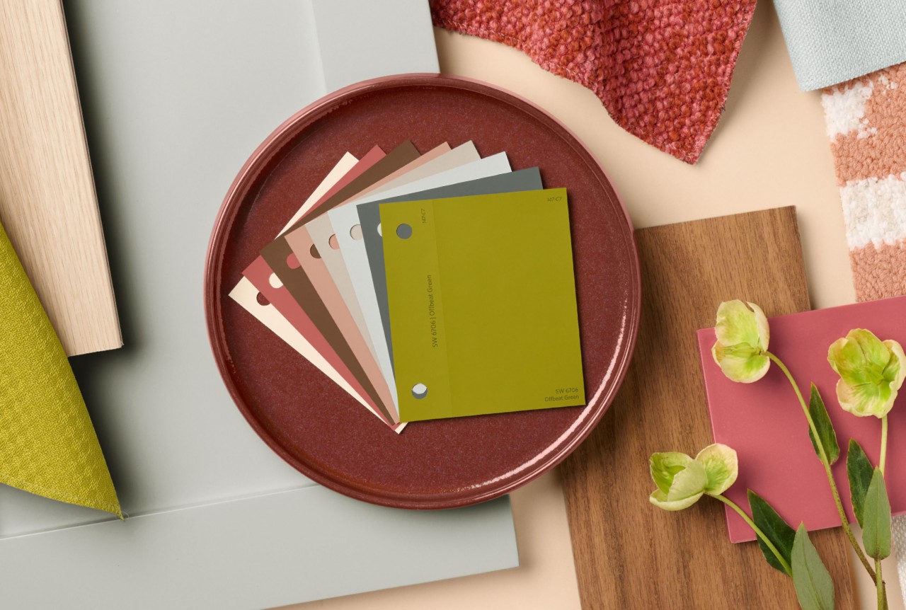 A round dish with paint color samples for The Loneliest Color 2026 coordinating palette surrounded by various materials and textures on a neutral background.