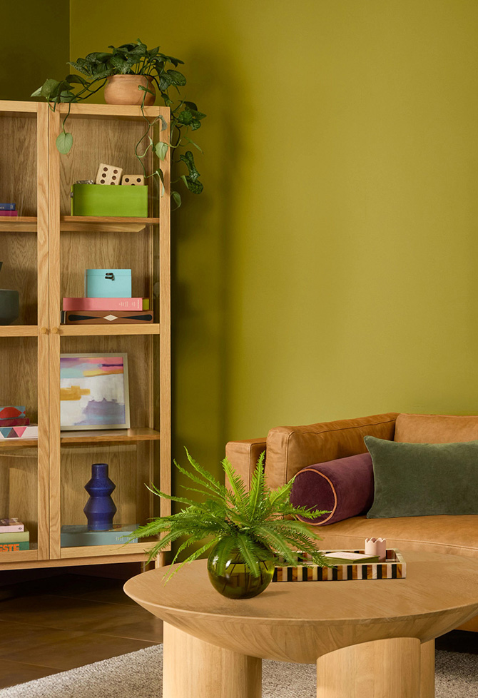 An Offbeat Green living room with a leather couch, colorful artwork, and wooden coffee table.