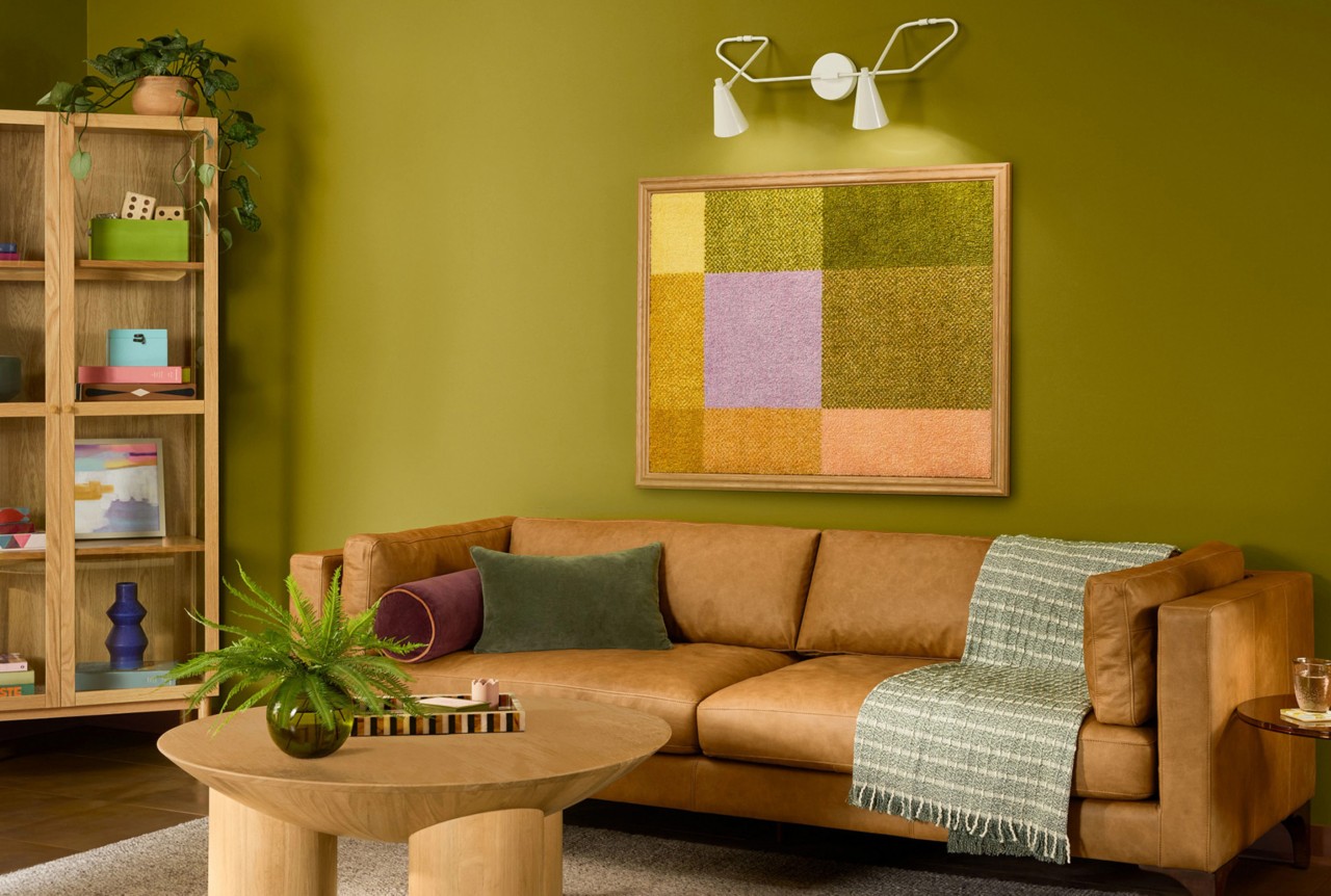 An Offbeat Green living room with a leather couch, colorful artwork, and wooden coffee table.