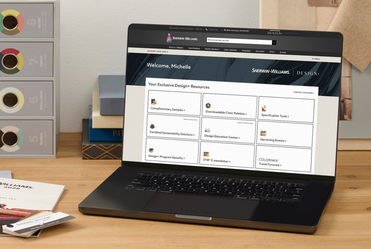 An open laptop and Sherwin-Williams color tools on a wooden desktop with the Design+ dashboard featured on screen.