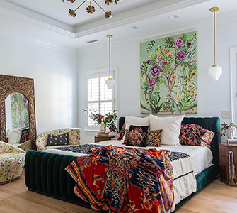 A bedroom with a large bed with a colorful patterned comforter against white walls.