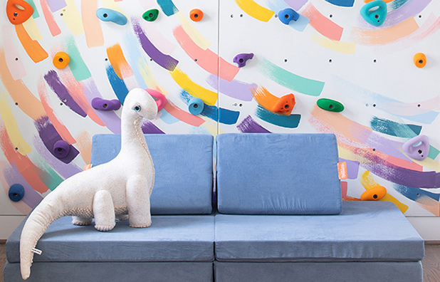 A toy dinosaur on a futon in front of a climbing wall.