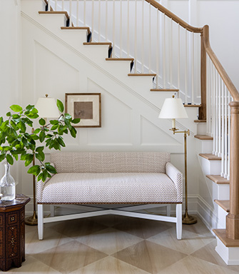 A nook at the bottom of a flight of stairs with a bench and lamp. The wall is painted with Cotton SW 9581.