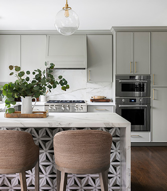 A kitchen with an island with white marble countertops and barstools. 