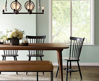 A dining area with a wooden table and chairs. The wall is painted with SW 9656 Pine Frost; a bluish green hue.