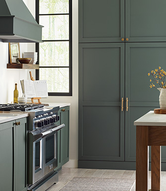 A kitchen with a steel stove and floor to ceiling cabinets painted with SW 9650 Succulent; a medium shade of green.