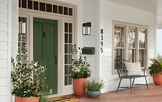 Front of a house with a porch, white siding and green front door.