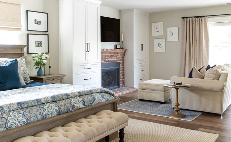 Traditionally styled room with wood floors, a neutral and blue color scheme, bed, fireplace and seating area.