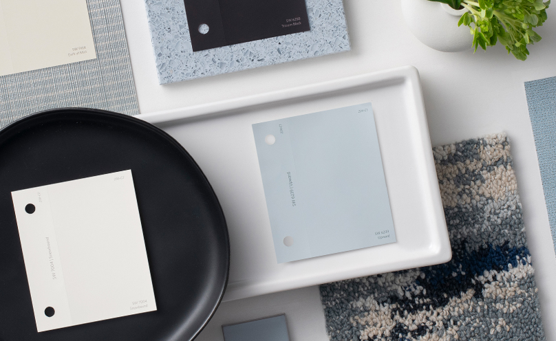 Flat lay with paint chips featuring the Sherwin-Williams Color of the Year, Upward, and its coordinating colors with flooring and wall samples, plates and trays, and other decorative elements arranged neatly.