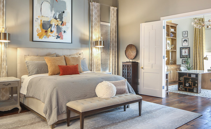 Inviting bedroom with adjoining home office space through open double doors with a neutral color scheme, unique artwork and furnishings.