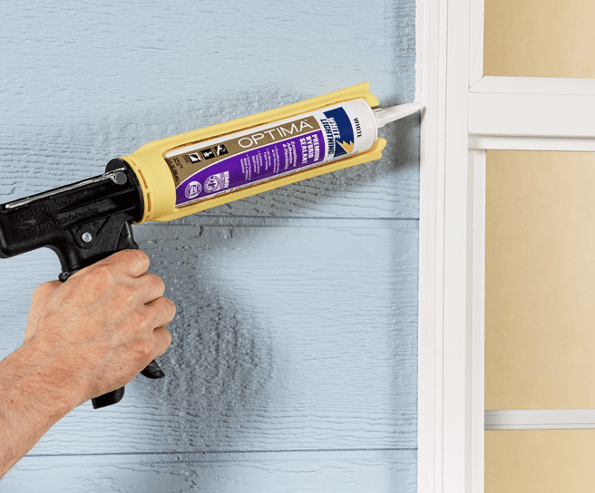 A person caulking a window.