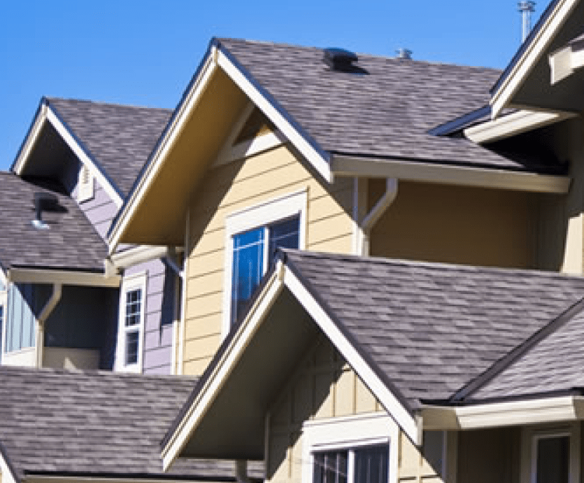 A house exterior painted tan with a gray house in the background.