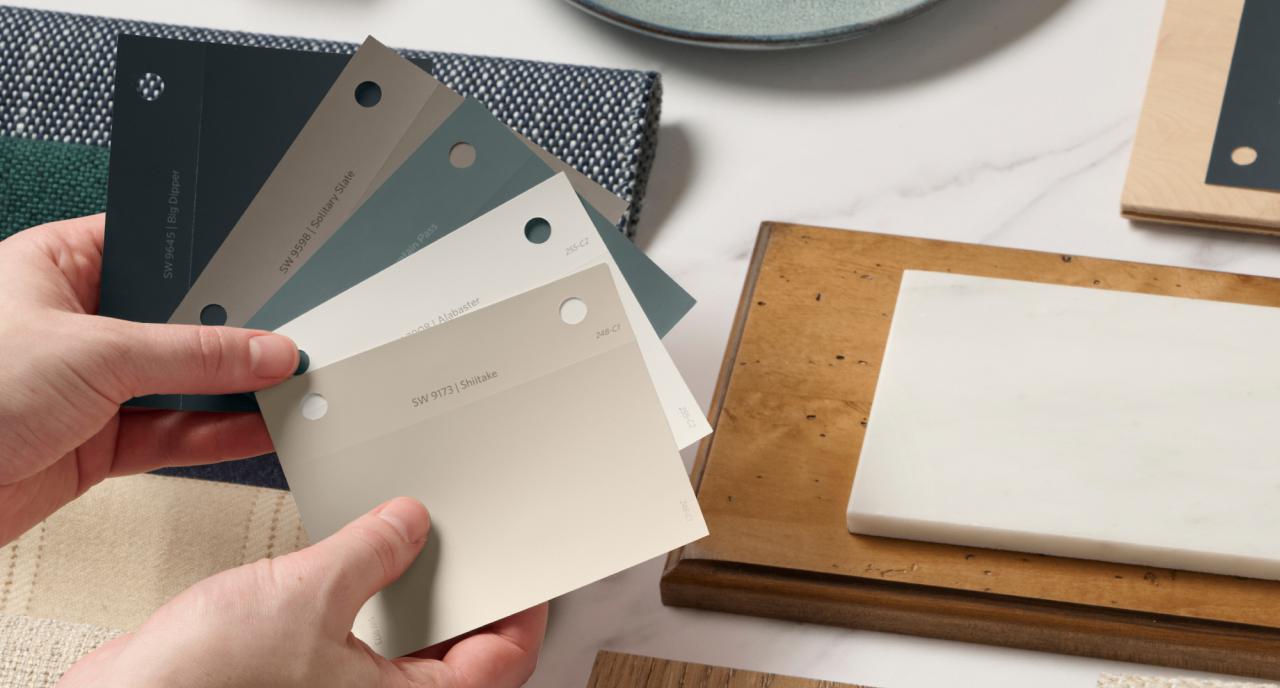 A person holding paint samples above a design board.