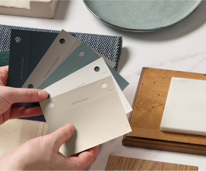 A person holding paint samples above a design board.