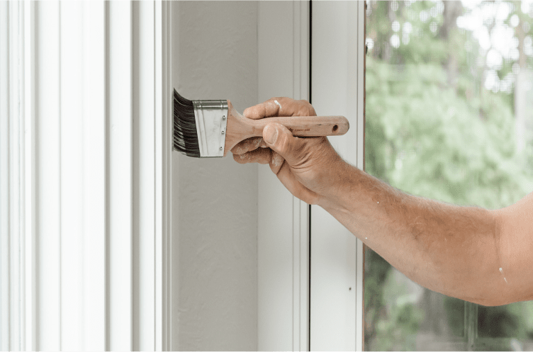 A person painting interior trim with a brush.