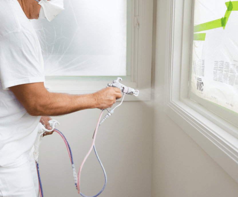 A person spraying paint on interior window trim.