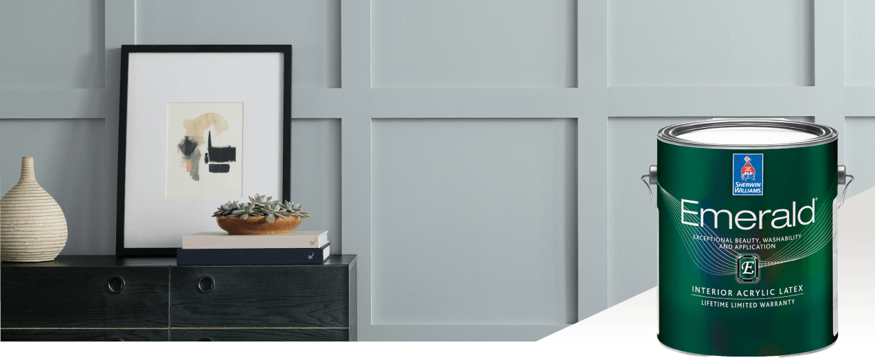 A wall painted light gray with a black side table with decor and a can of Emerald interior paint.