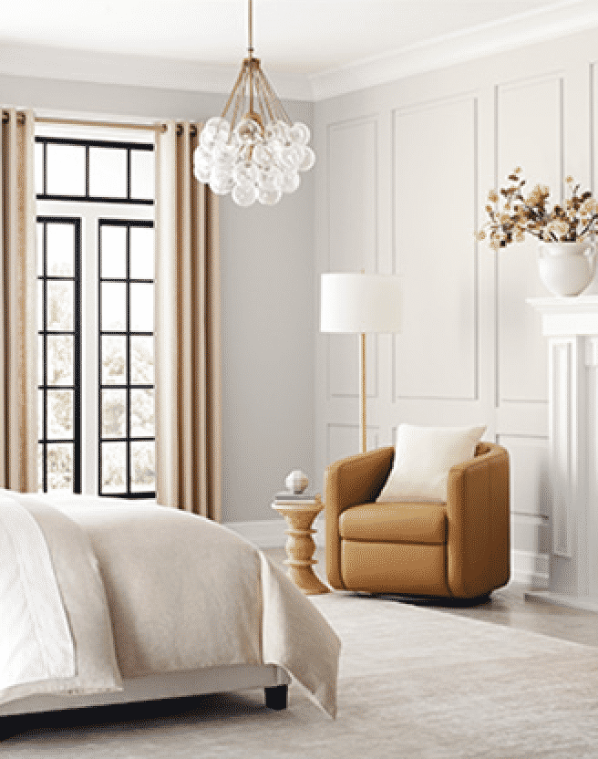 Bright, neutral bedroom with standing lamp, chair, large window with drapes.