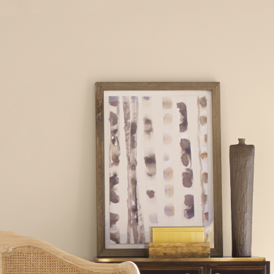 Beige walls painted Drift of Mist SW 9166 with a light woven chair and a small table with an abstract print in a simple gold frame, a tall vase, and two stacked small boxes.