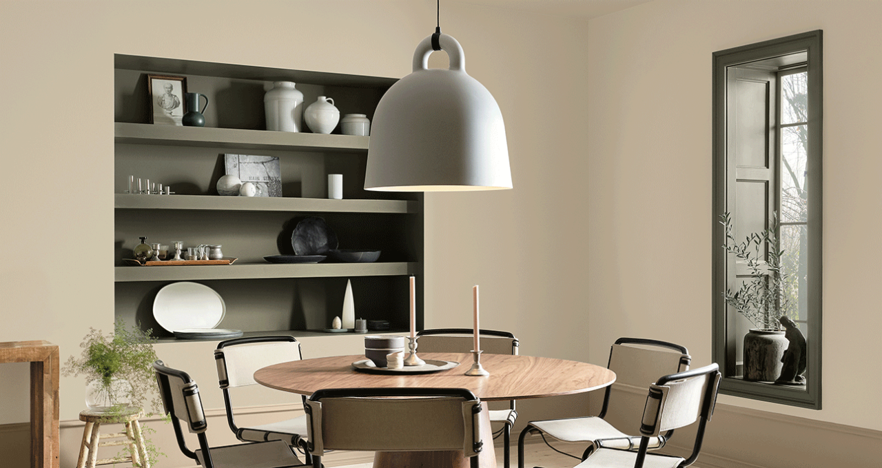 A beige dining room painted Polished Mahogany SW 2838 with recessed built-in shelves and a recessed window with décor on the ledge. There is a round table with a large pendant light overhead and six chairs.
