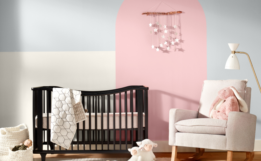 Nursery with a neutral chair, black crib, small toys on the ground, and walls painted blue, pink, and white.