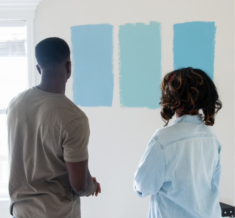 Two people looking at three different blues painted on a white wall.