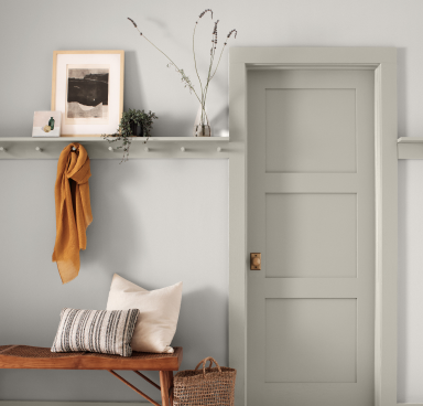 A light gray entryway with wooden side table and shelf with a jacket hanging