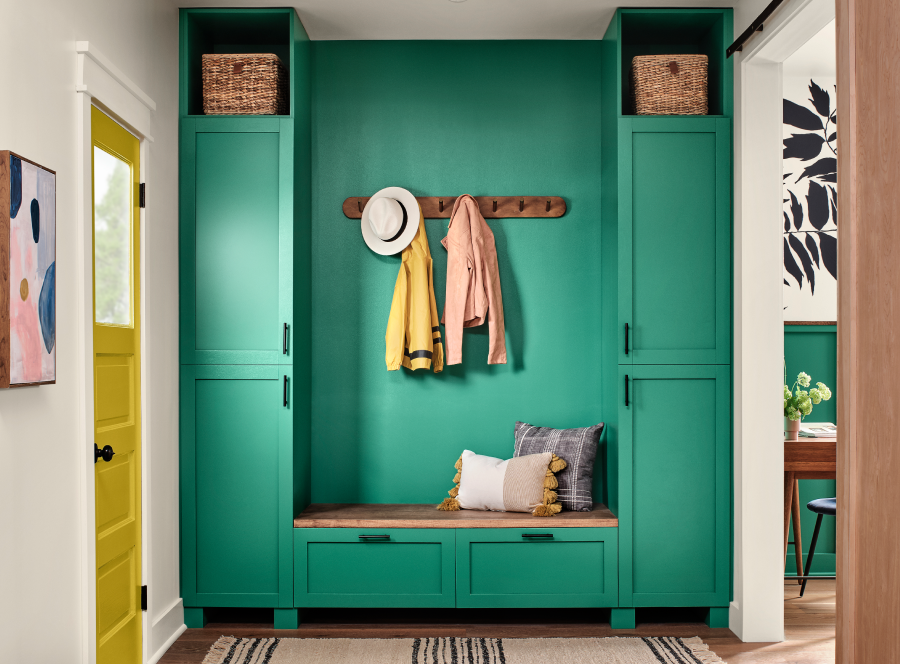An entryway with green sitting area and clothes hanging on wall hooks