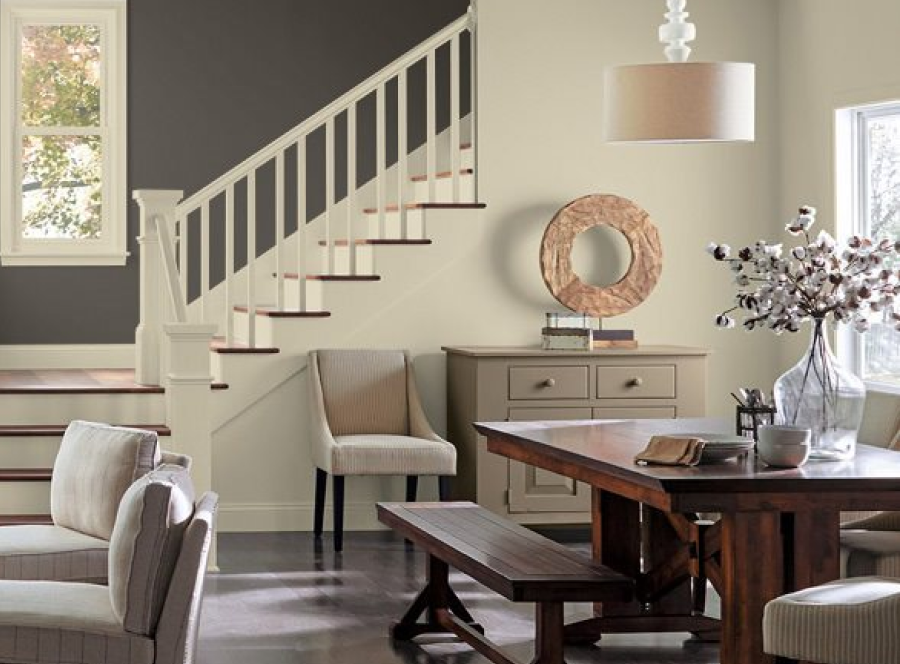 A stairway and dining room with neutral colors, farm table and bench