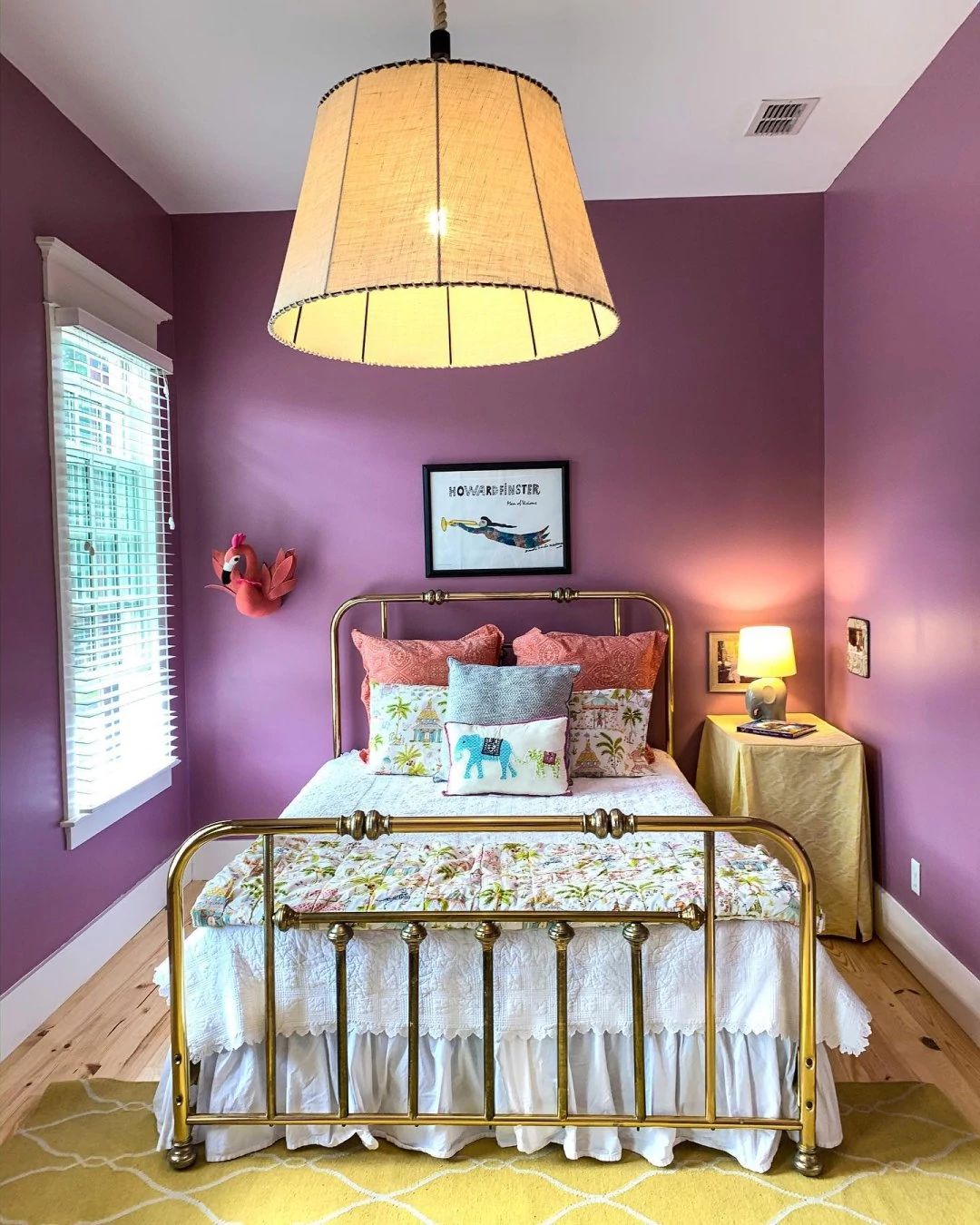 A bedroom painted Thistle SW 6283 with a brass bed in the middle and a large pendant light overhead.