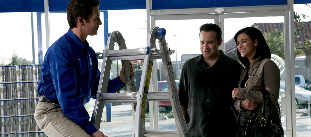 A Sherwin-Williams employee is helping a couple shop for a paint ladder.