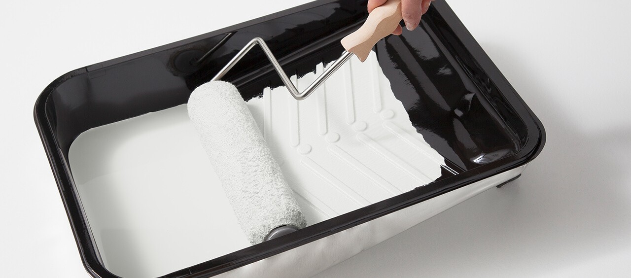 A paint tray with white paint and a paint brush.