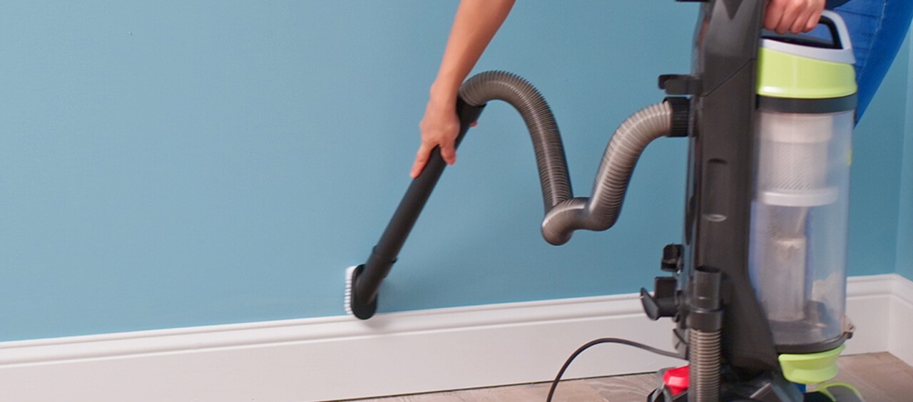 A person is using a vacuum to clean dust off a wall.