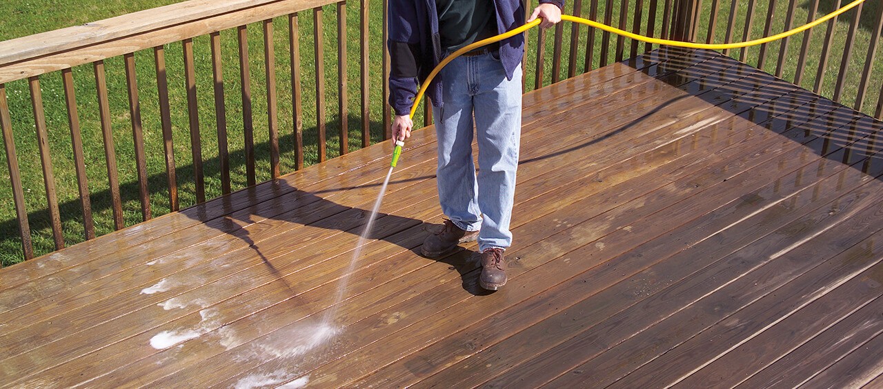 A man rinsing a deck to prepare for staining.